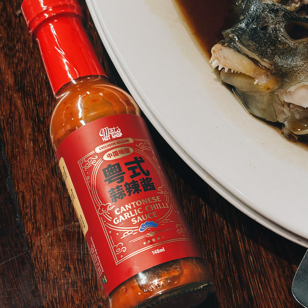 Bottle of Cantonese Garlic Chilli Sauce on a wooden surface with a plate of fish.