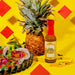Pineapple with a bottle of hot sauce on a yellow background